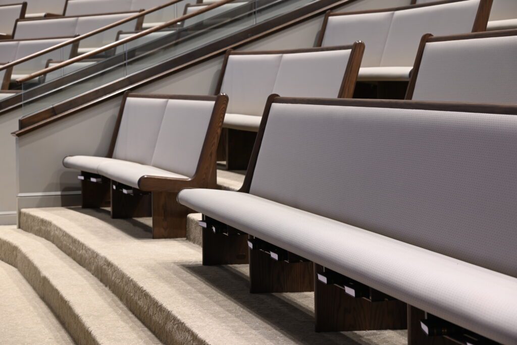 A row of white-cushioned pews in the balcony of a church.